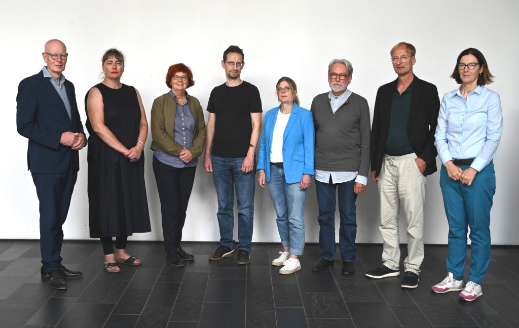 Gruppenbild der Mitglieder der Kommission vor einer weißen Wand.